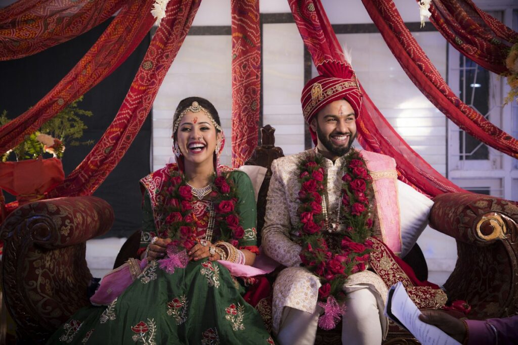 Smiling bride and groom in traditional wedding attire; groom wearing a ceremonial cap